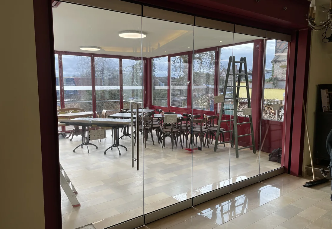 Mehrteilige transparente Glas-Schiebewand vor einem gastronomisch genutzten Raum